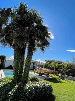 A poolside area with a palm tree, a boat, and a stone wall. - Escapades Océanes (Sainte-Marie-de-Ré)