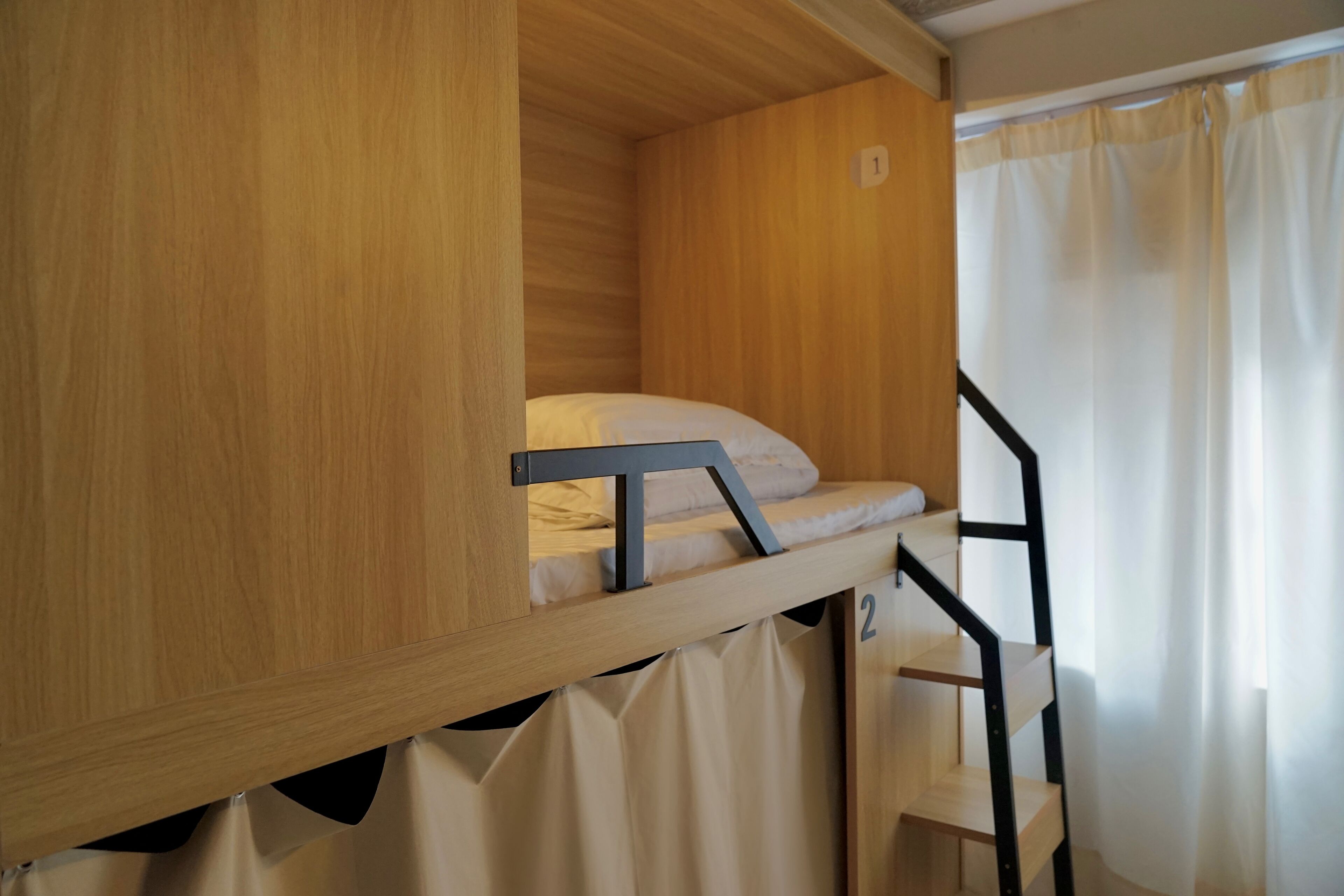 A bunk bed with a wooden frame, a mattress, and a pillow. There is a number '1' on the wall above the bed.