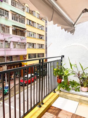 A balcony with a metal railing, potted plants, and a view of a street with cars and buildings. - Waveflo Hostel (Kowloon)