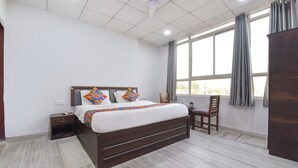 A hotel room with a large bed, a desk, and a chair. There is a window with curtains and a view of buildings outside. - Fabhotel Connect (Jaipur)