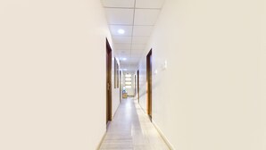 A long, narrow hallway with light-colored walls and a wooden floor, leading to a door at the end. - Fabhotel Connect (Jaipur)
