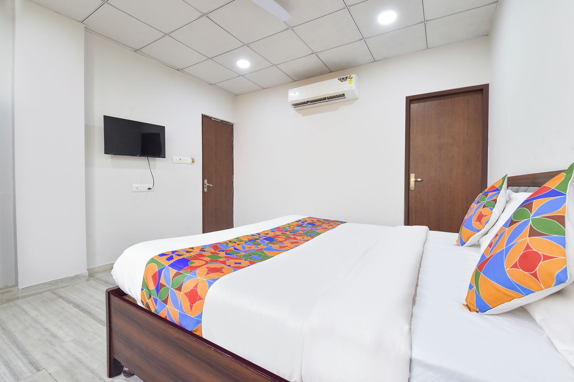 A bedroom with a bed, a TV mounted on the wall, and an air conditioning unit.