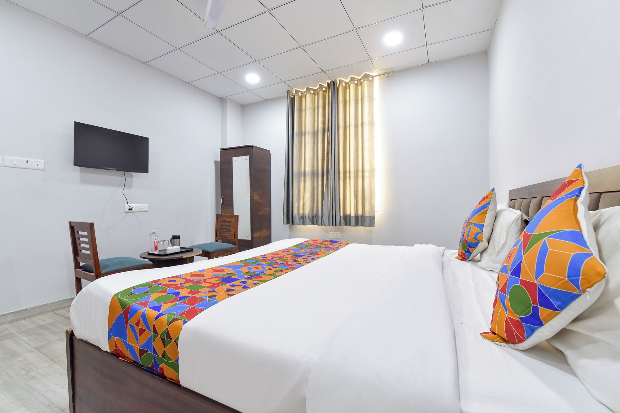 A hotel room with a bed, a desk, a chair, a wardrobe, a television, and a window with curtains.