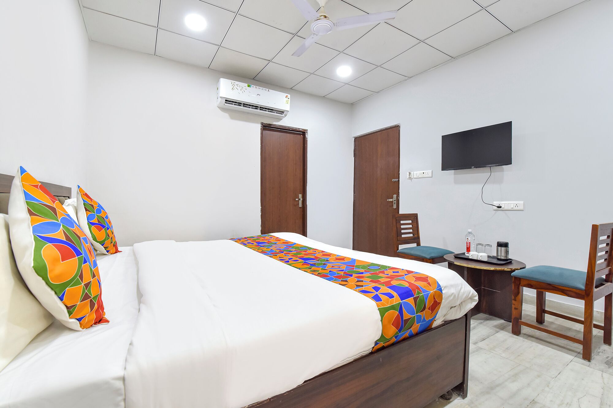 A hotel room with a bed, a desk, a chair, a TV, an air conditioner, and a door.