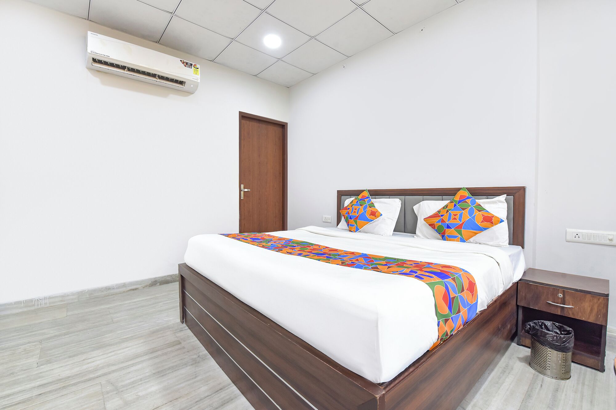 A hotel room with a wooden bed, white bedding, and a colorful throw blanket.
