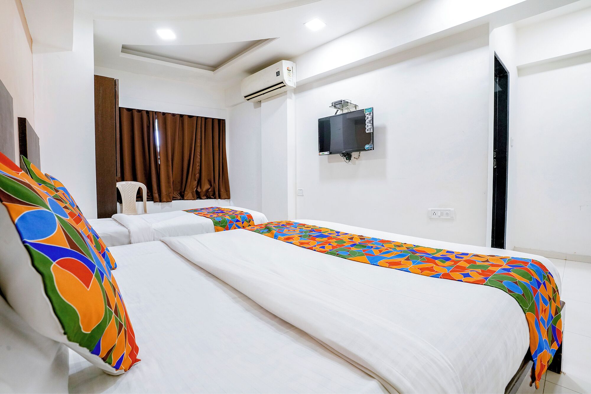 A hotel room with two beds, a TV on the wall, and an air conditioning unit.
