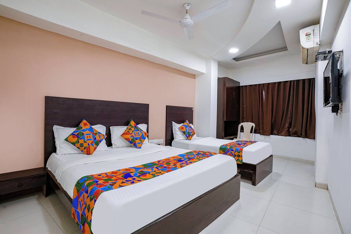 A hotel room with two beds, a ceiling fan, an air conditioning unit, and a window with curtains.