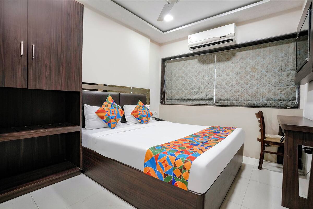 A bedroom with a bed, a wardrobe, a desk, and an air conditioning unit.