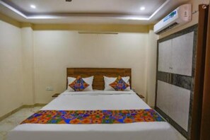 Habitación de hotel con cama, cabecera de madera, colcha colorida y equipo de aire acondicionado.
