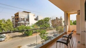 A balcony with a view of a road and buildings, a dining area with chairs, and a door leading to another room. - Fabhotel Starlight Sanctuary (Gurugram)