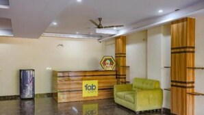 A reception area with a wooden reception desk, a green sofa, and a logo on the wall. - Fabhotel Starlight Sanctuary (Gurugram)