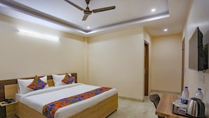 A hotel room with a bed, a desk, a chair, a ceiling fan, and a TV. - Fabhotel Starlight Sanctuary (Gurugram)