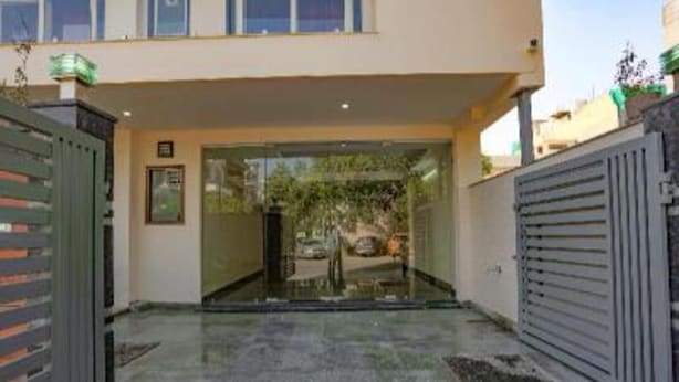 A modern building entrance with a glass door, a metal gate, and a paved driveway. - Fabhotel Starlight Sanctuary (Gurugram)