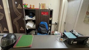 Ein Schreibtisch mit einem Helm, einer grünen Ordner und einem blauen Stuhl. Ein Schild an der Tür weist auf die Zimmernummern hin.