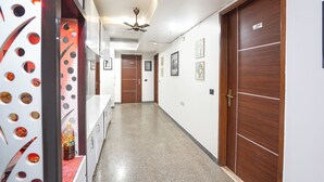 A hotel corridor with wooden doors, a ceiling fan, and framed pictures on the walls. - Fabhotel Golden Eye Inn (New Delhi)