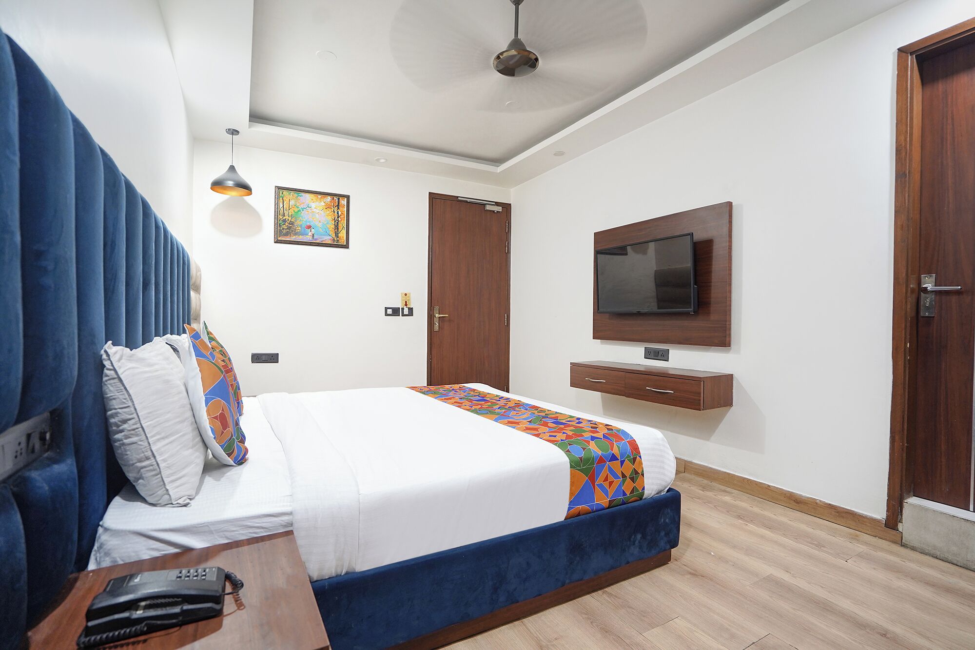 Una habitación de hotel con una cama, un televisor en la pared, un ventilador de techo y una puerta.