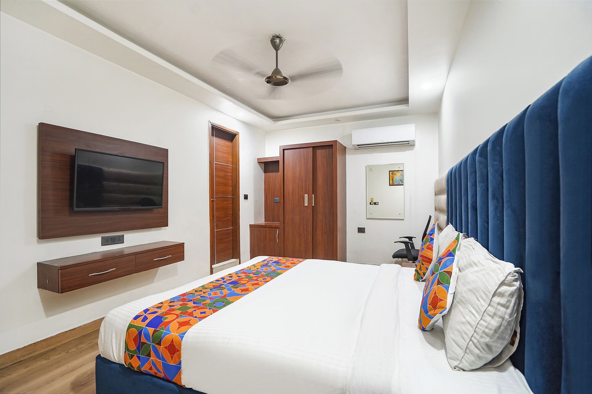 Een moderne slaapkamer met een flatscreen-tv, een plafondventilator, een kledingkast en een bed met een kleurrijk dekbed.