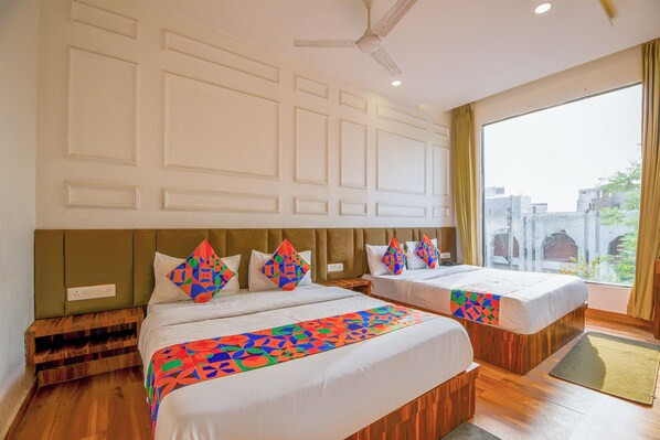 Habitación de hotel con dos camas, ventilador de techo y un ventanal con vistas a edificios.