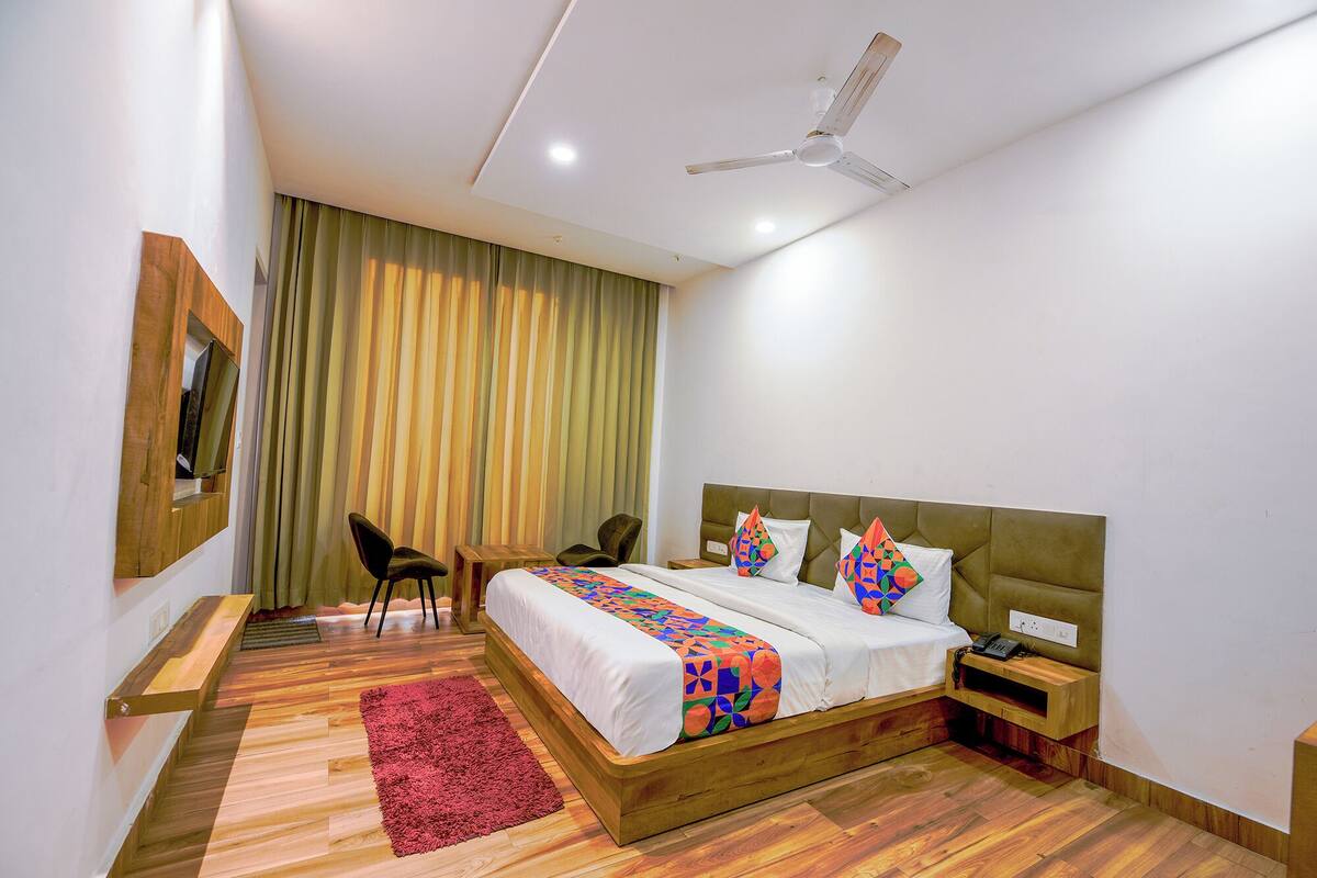 Une chambre d’hôtel moderne avec un lit en bois, un tapis rouge, un ventilateur de plafond et un téléviseur fixé au mur.