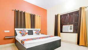 A bed with a patterned bedspread, a bedside table, a wall socket, and an air conditioning unit. - FabHotel RB Palace - Nr. Varanasi Junction (Cantt) Railway Station (Varanasi)