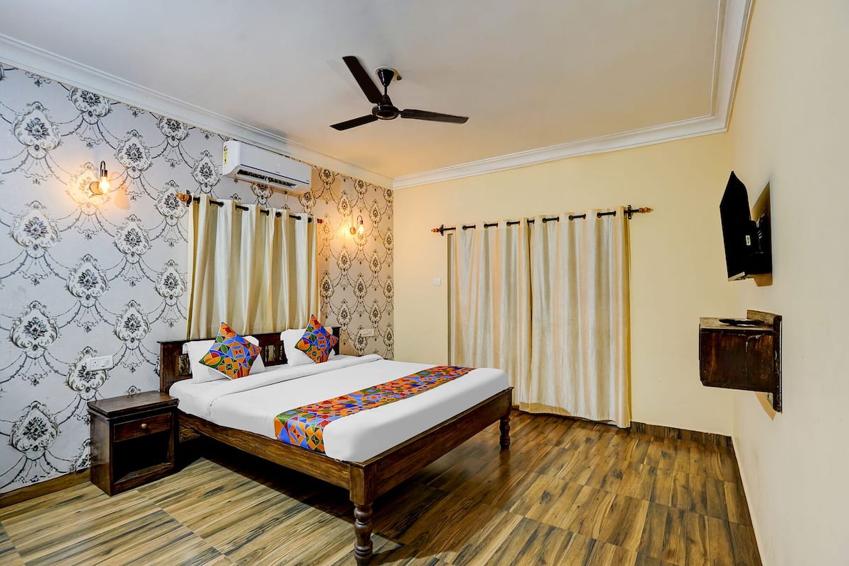 A bedroom with a wooden bed, patterned wallpaper, a ceiling fan, an air conditioning unit, and curtains.