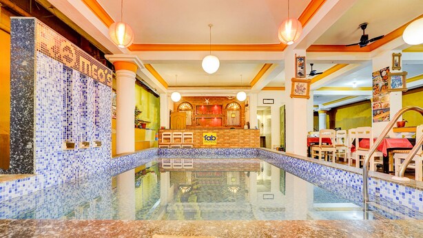 A hotel lobby with a central pool, a reception desk, and a dining area.