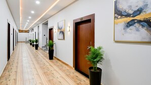 A long, narrow hallway with wooden flooring, black potted plants, and framed artwork on the walls. - Fabhotel Padmakar Kashi (Varanasi)
