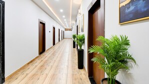 A long, narrow hallway with wooden flooring, multiple doors, and potted plants. - Fabhotel Padmakar Kashi (Varanasi)