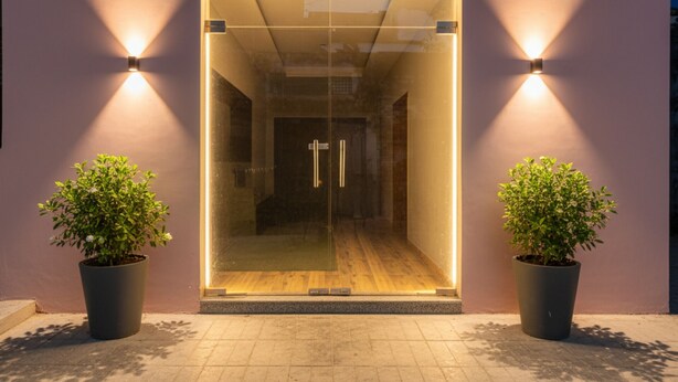 A modern entrance with a glass door, two potted plants, and wall-mounted lights. - Fabhotel Padmakar Kashi (Varanasi)