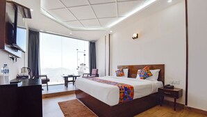 A hotel room with a large bed, a desk with a chair, a bedside table, and a view of the outdoors. - Fabhotel Burans Residency (Dhanaulti)