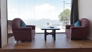 A room with two armchairs and a small table, large windows with a mountain view, and a curtain on the right. - Fabhotel Burans Residency (Dhanaulti)