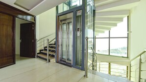 A modern interior with a staircase, a glass elevator, and a view through a large window. - Fabhotel Burans Residency (Dhanaulti)