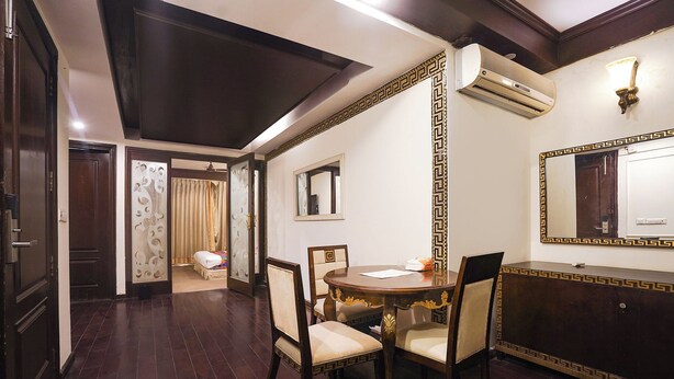 A room with a wooden floor, a round dining table with chairs, a large mirror, and an air conditioning unit on the wall. - Fabhotel Nfc Royale (New Delhi)