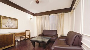 A living room with a brown leather sofa, a glass coffee table, a wooden desk with a chair, and a painting on the wall. - Fabhotel Nfc Royale (New Delhi)