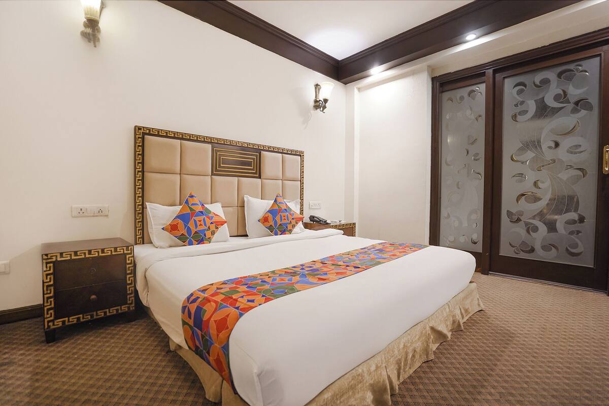 A hotel room with a large bed, a nightstand, a decorative wall panel, and a door with intricate designs.