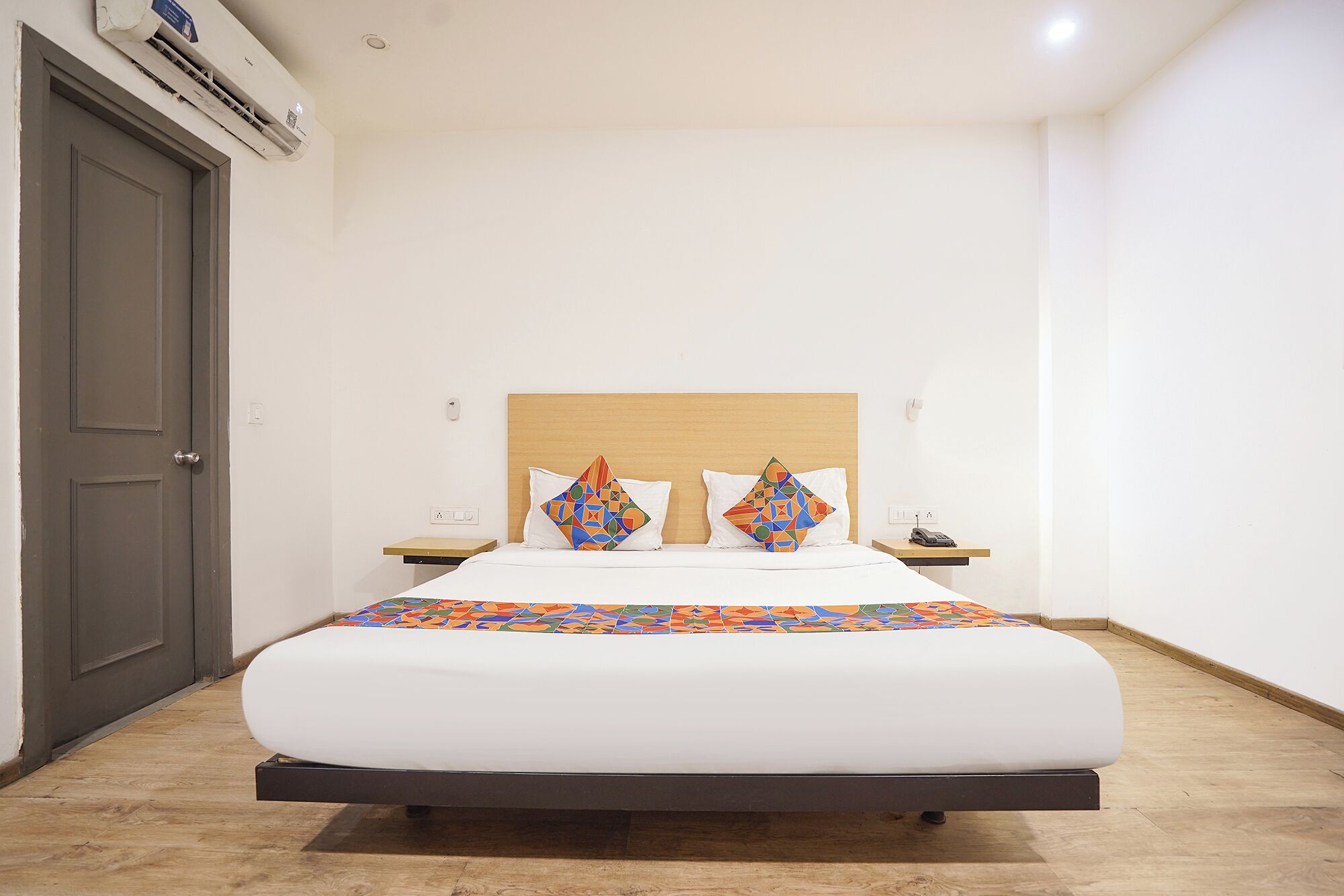 A hotel room with a bed, a nightstand, a phone, and an air conditioning unit.