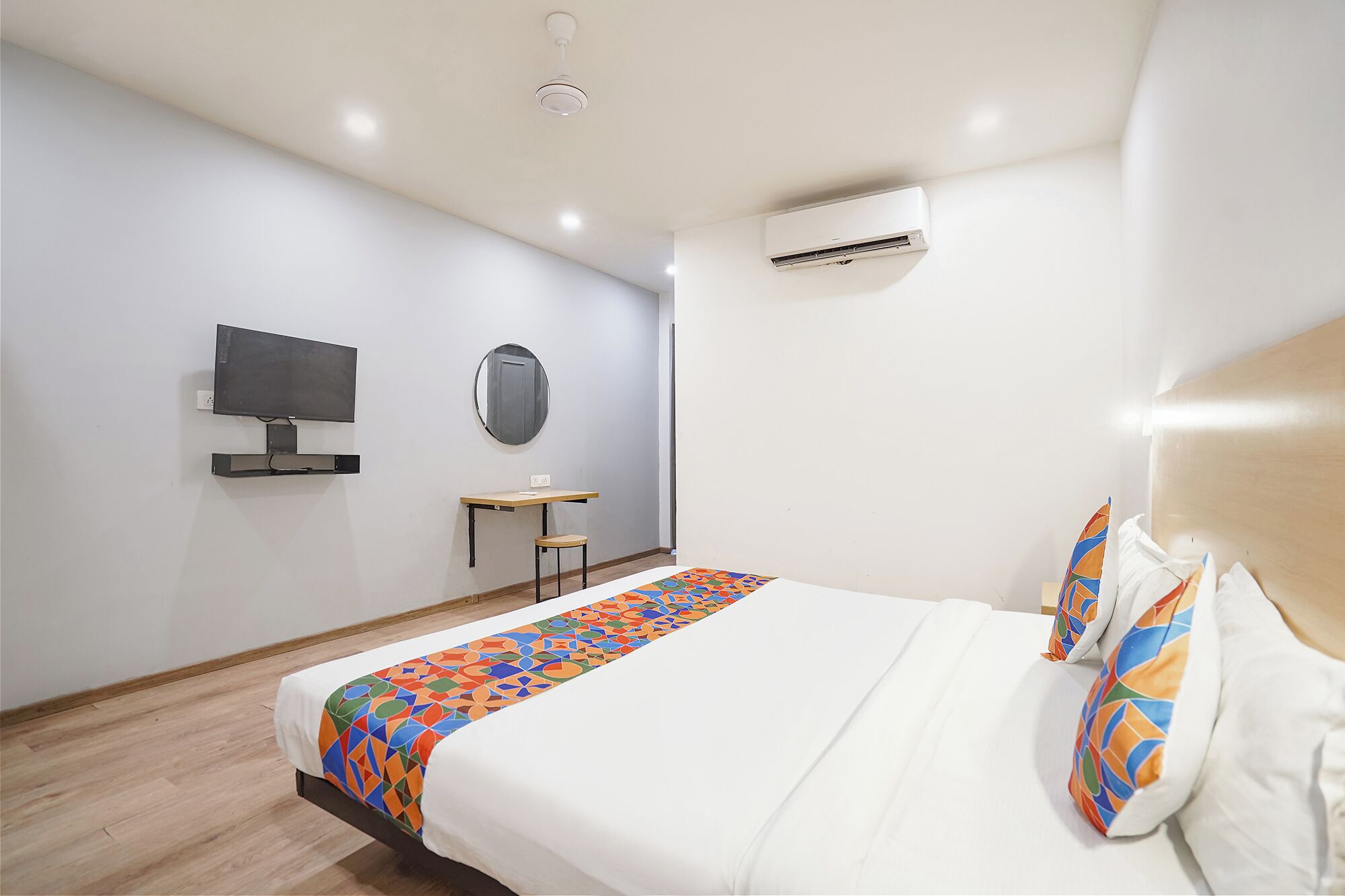 A hotel room with a bed, a desk, a chair, a television, and an air conditioning unit.