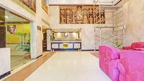 Una hall d'albergo con una reception, un orologio, un bar e un'ampia parete decorativa.