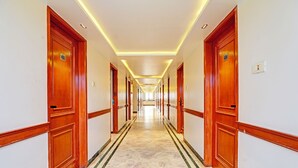 Un corridoio d'albergo con porte in legno, pavimento in marmo e illuminazione incassata.