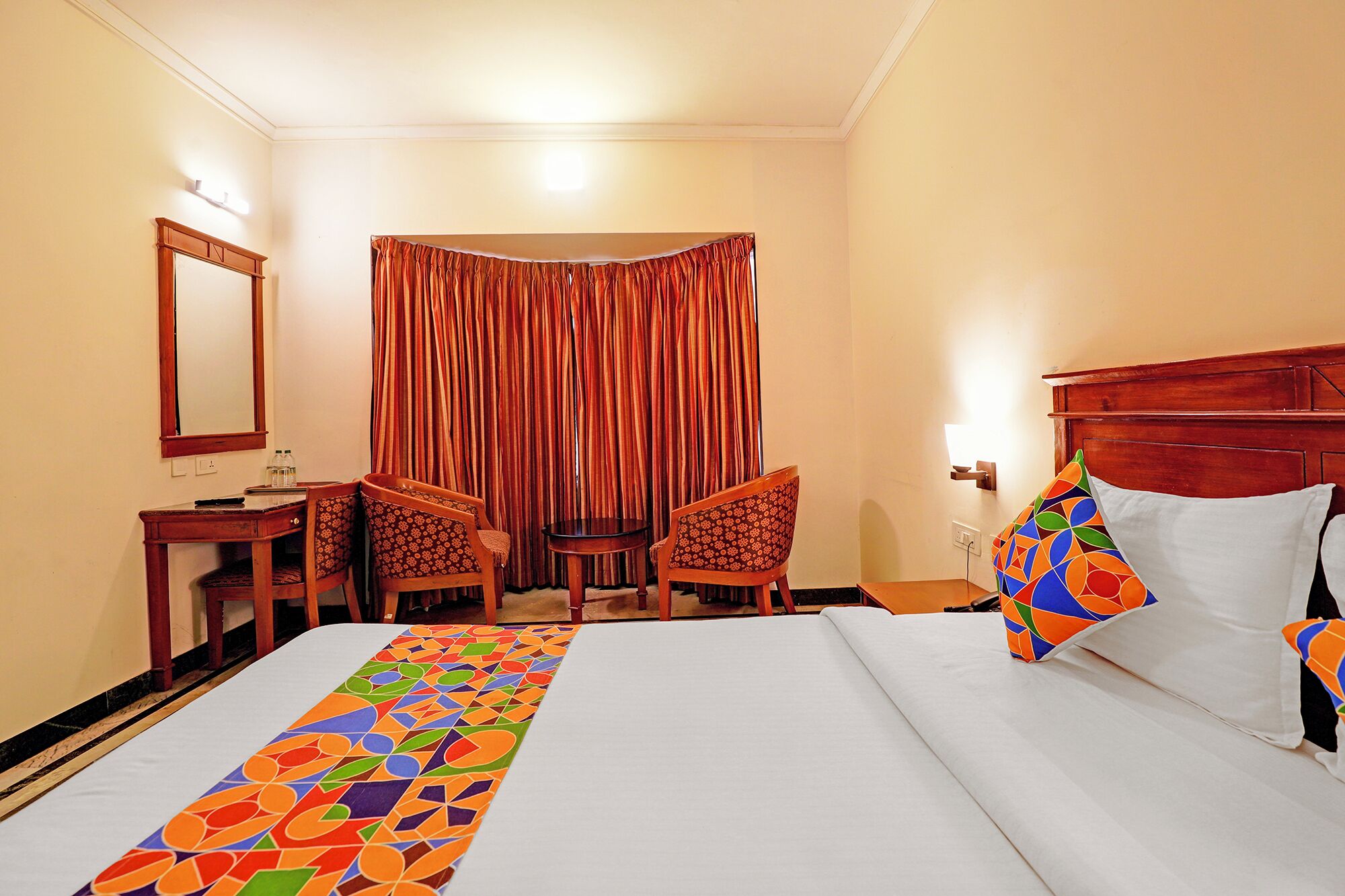 A hotel room with a bed, two chairs, a small table, a mirror, and a curtain.