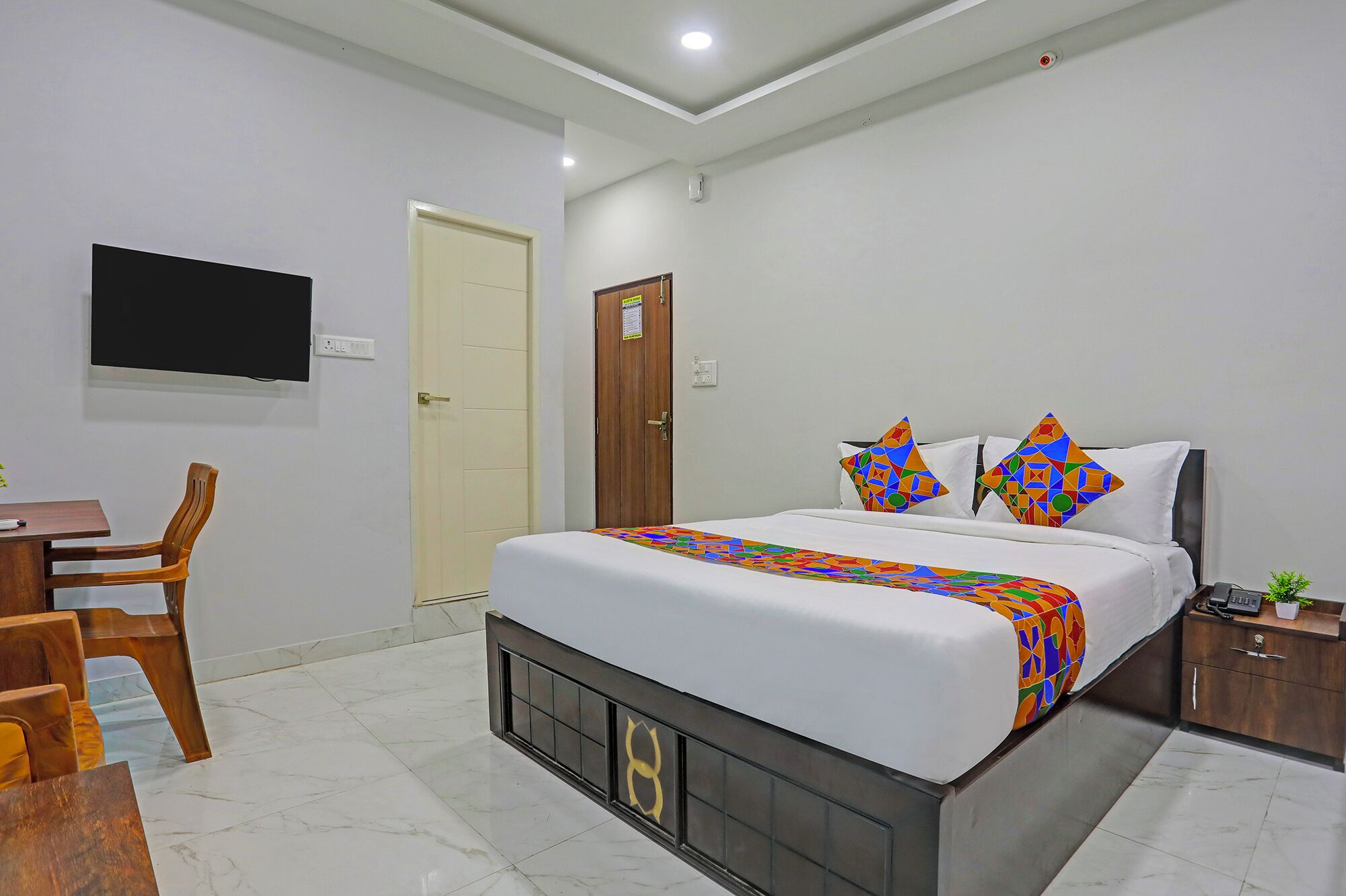 A hotel room with a bed, a desk, a chair, a TV, and a door.