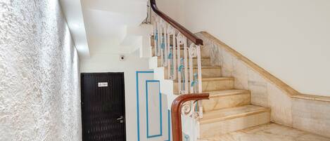 A staircase with marble steps and a wooden handrail, leading to a black door with a sign.
