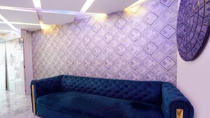 A modern interior with a teal velvet sofa, patterned wallpaper, and a geometric light fixture. - Fabhotel 7 Am (Mumbai)