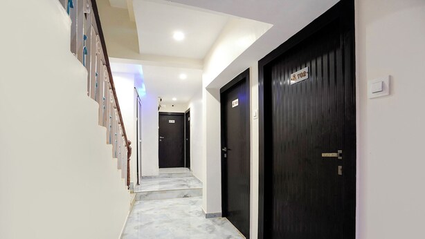 A hallway with a marble floor, black doors, and a staircase with white walls and blue accents. - Fabhotel 7 Am (Mumbai)