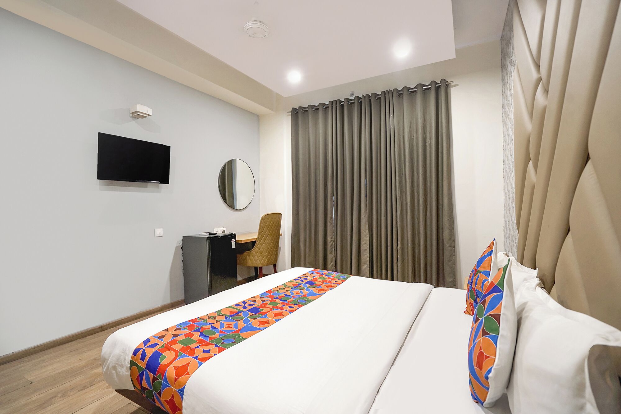 A hotel room with a bed, a desk, a chair, a television, and a window with curtains.