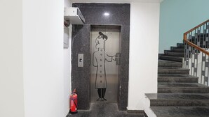 A modern elevator with a marble finish, a fire extinguisher, and a staircase with wooden railings. - FabHotel Novis Stayz (Noida)