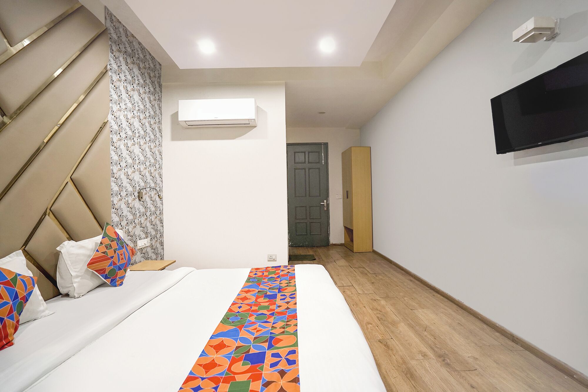 A bedroom with a bed, a TV mounted on the wall, and an air conditioning unit.
