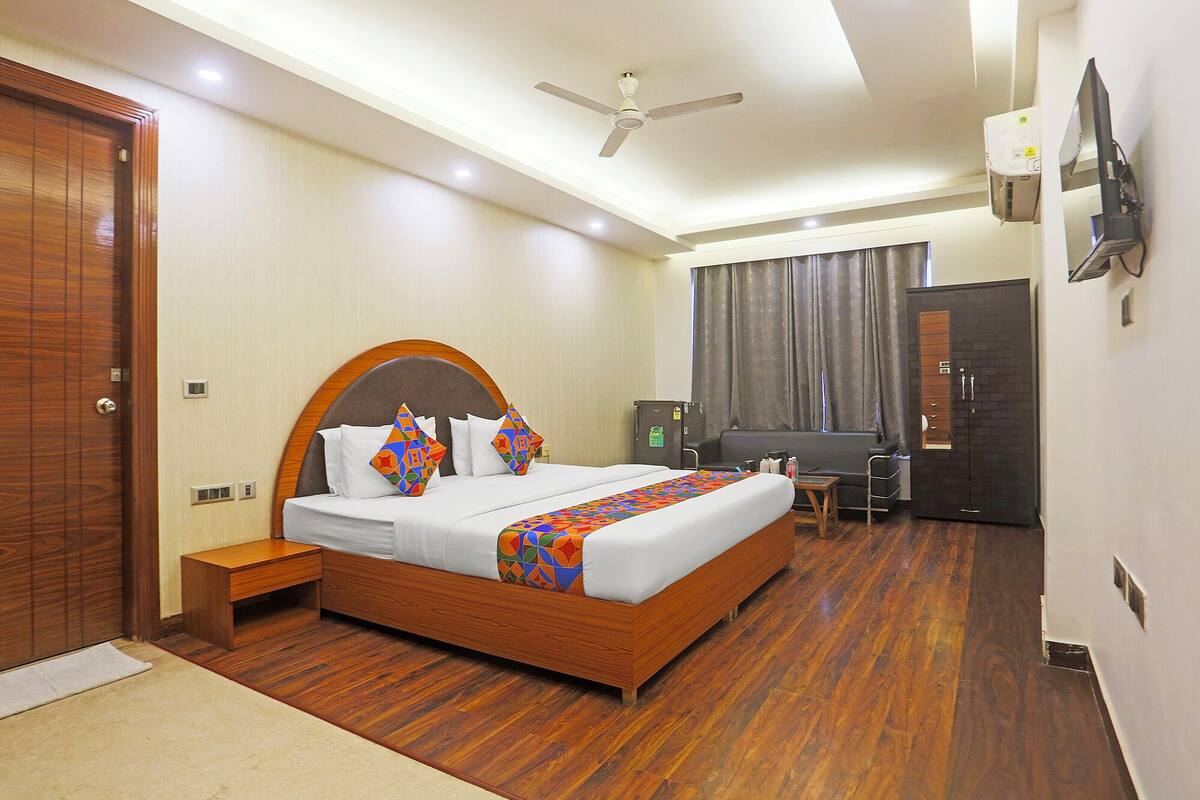 A hotel room with a wooden bed, a desk, a wardrobe, a ceiling fan, and a TV.
