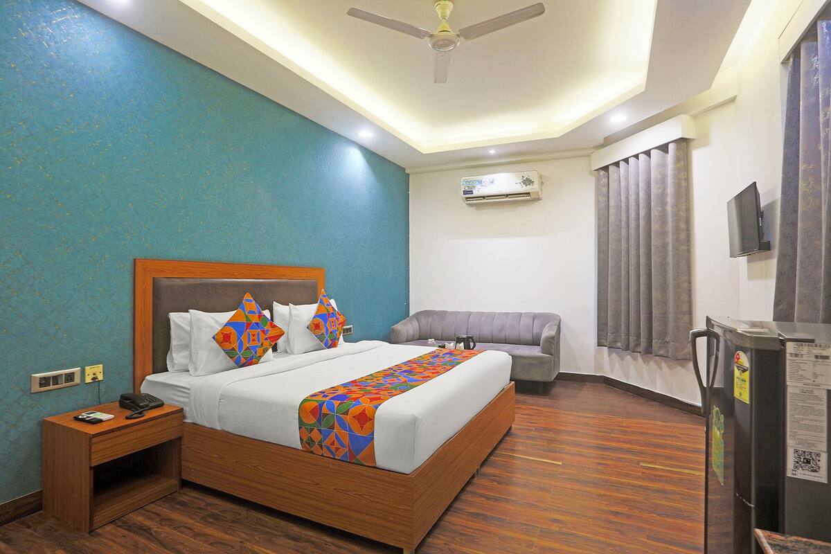A hotel room with a wooden bed, a grey sofa, a TV, and an air conditioning unit.