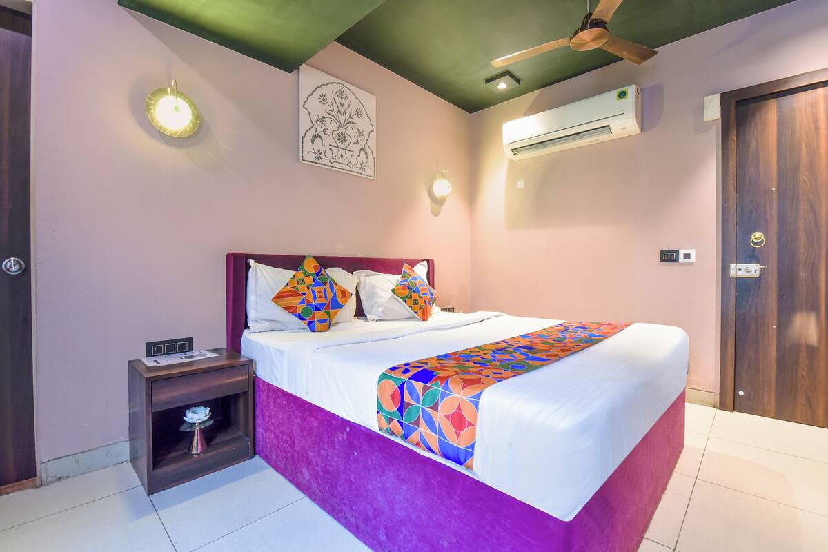 A neatly made bed with colorful pillows, a bedside table with a lamp, and an air conditioning unit on the wall.